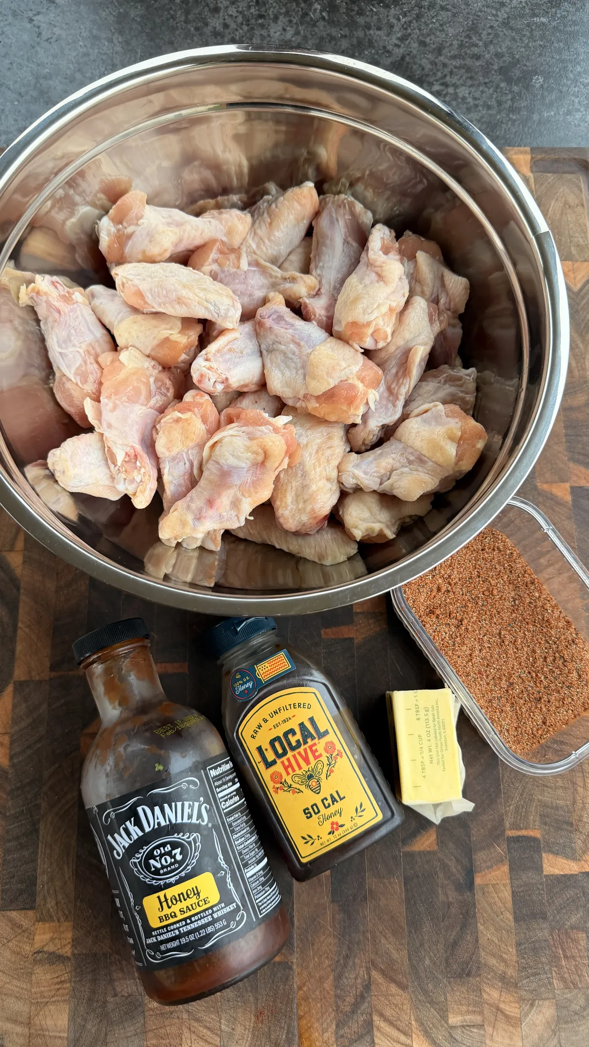 Raw chicken wings in steel bowl with honey BBQ sauce, Local Hive honey, butter, and chipotle seasoning on cutting board