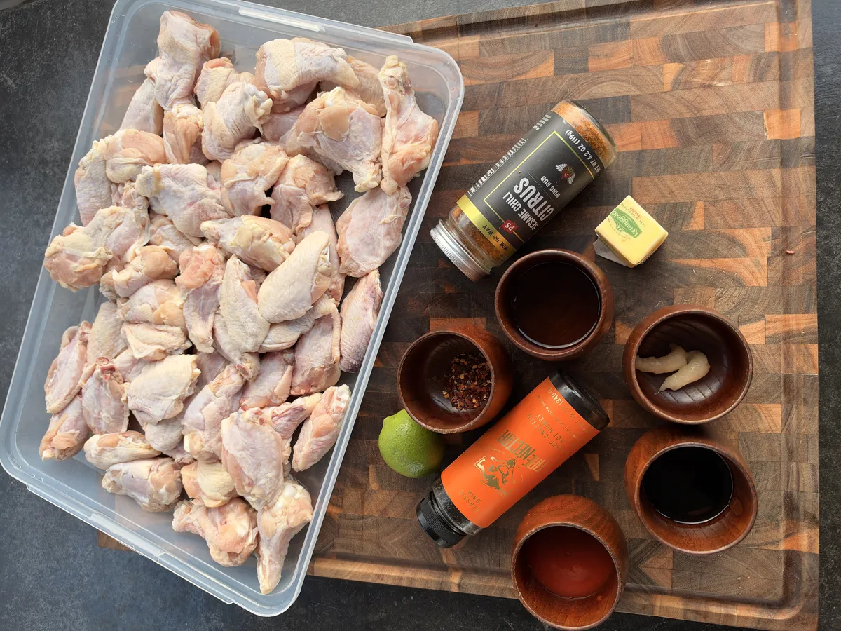 Raw chicken wings in container with hot honey lime sauce ingredients: honey, butter, soy sauce, red pepper flakes, lime, and garlic