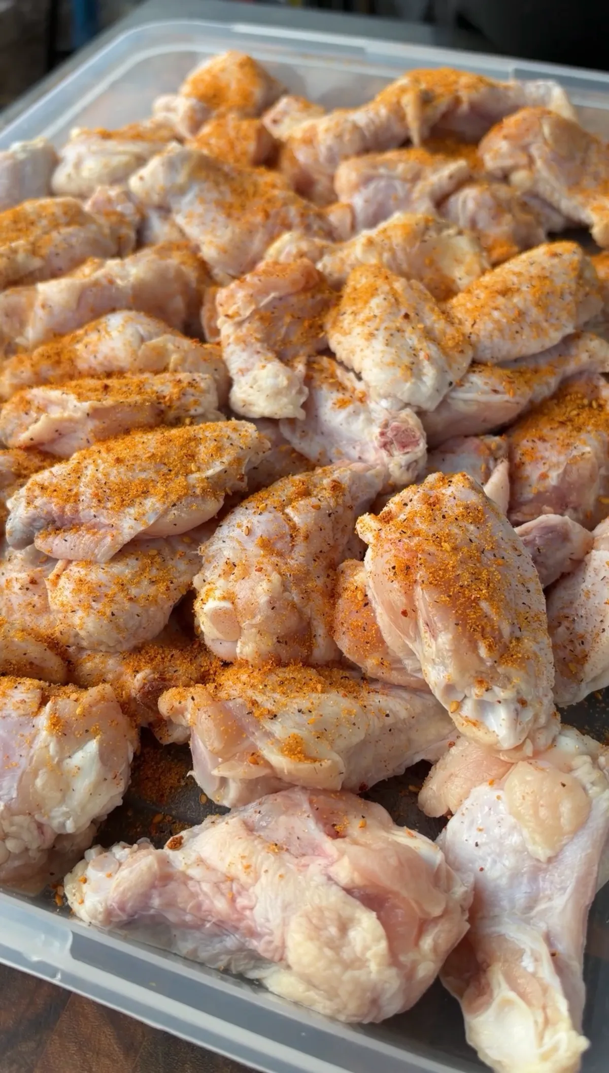Raw chicken wings coated with olive oil and seasoned with paprika, salt, and pepper in a clear plastic container