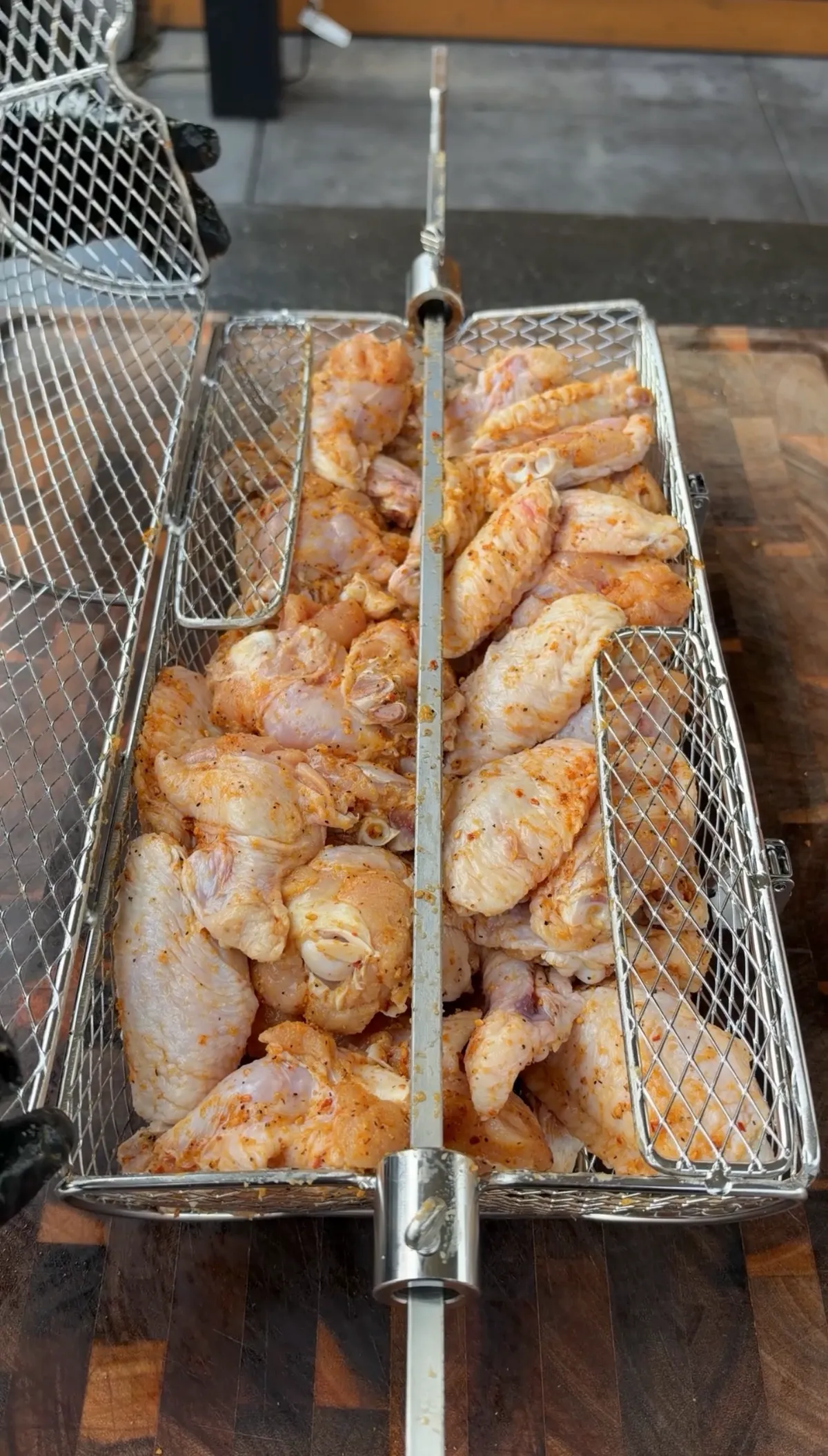 Raw chicken wings seasoned with paprika and olive oil loaded into a rotisserie basket ready to cook