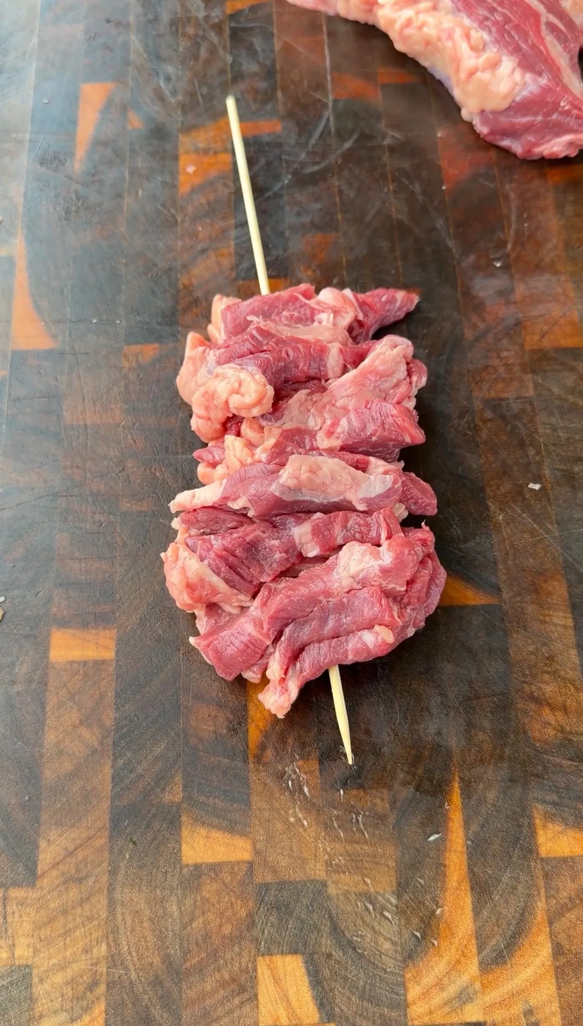 Thin-sliced tri-tip pieces threaded onto a soaked wooden skewer on a wood cutting board, ready to season