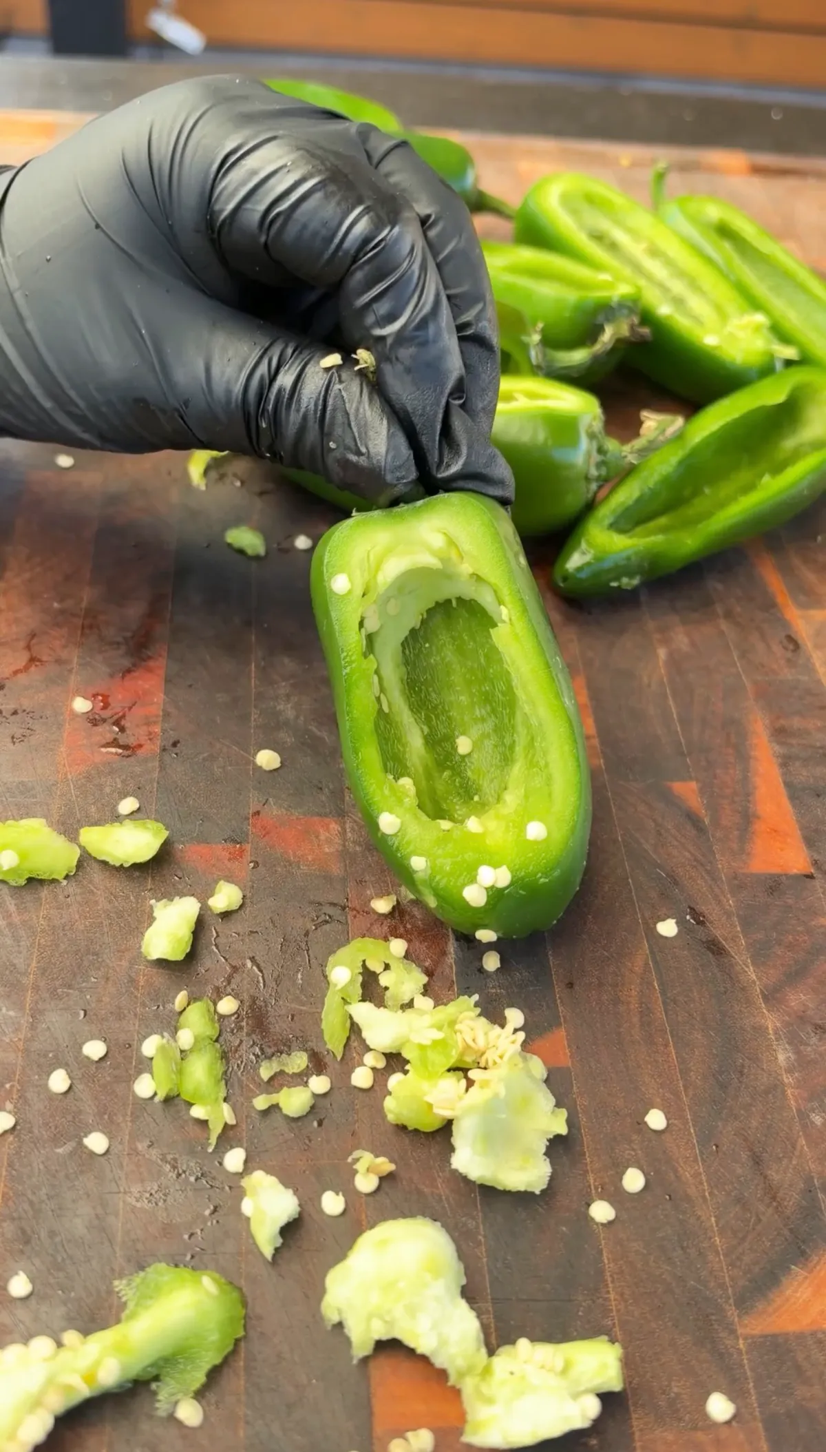 Gloved hand holding a hollowed jalapeño boat with seeds and veins removed on a wooden cutting board