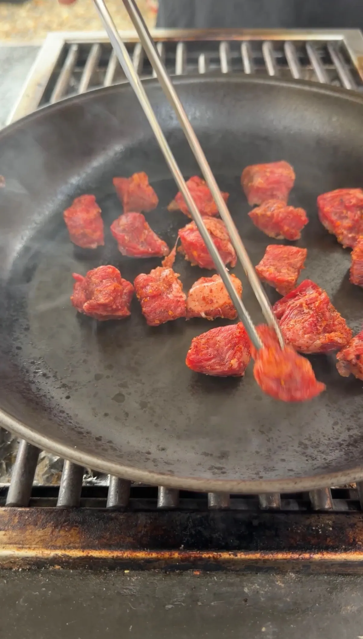 Seasoned ribeye steak bites searing in a single layer in a hot skillet, turned with tongs over high heat