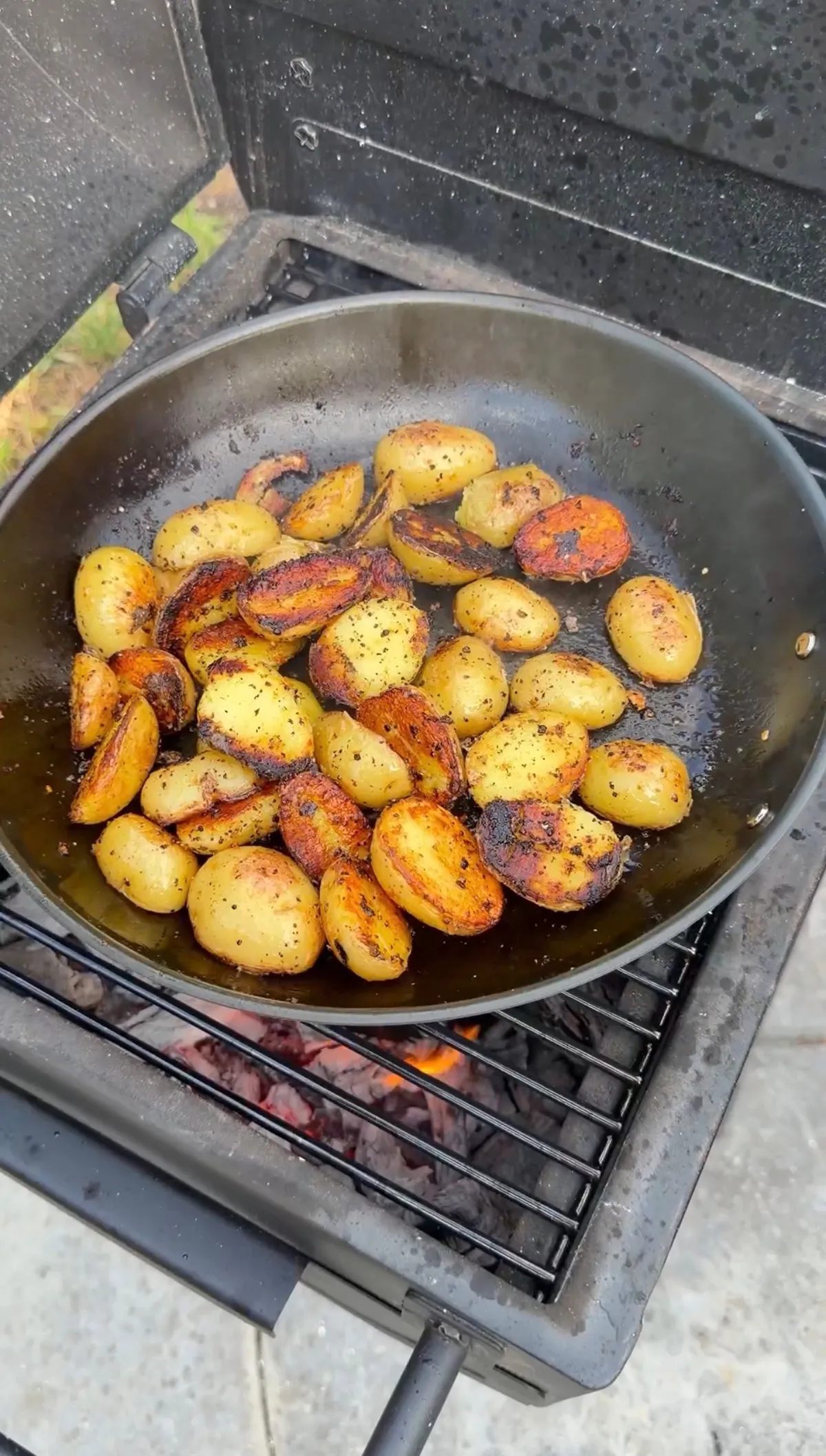 Baby potatoes halved and roasted with lemon pepper seasoning in a cast iron skillet over live charcoal grill