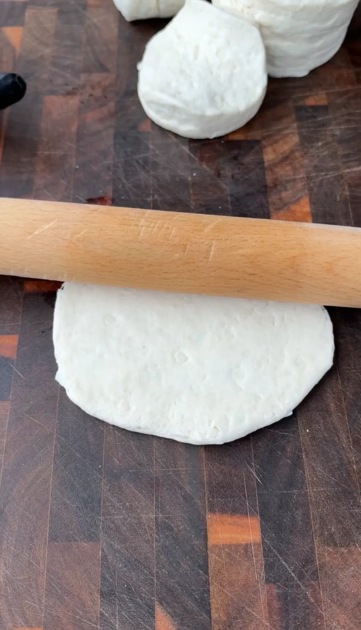 Pillsbury biscuit dough being rolled out with a wooden rolling pin on a butcher block cutting board