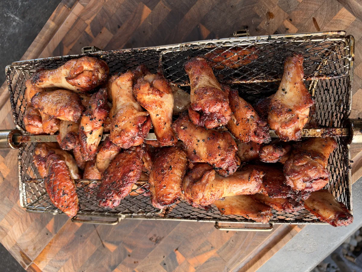 Crispy rotisserie chicken wings seasoned with paprika in a rotisserie basket on a wood cutting board