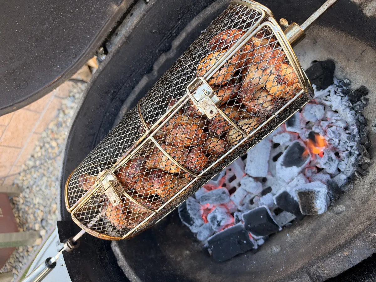 Chicken wings in a rotisserie basket spinning over glowing charcoal, skin golden brown and crisping to 185°F