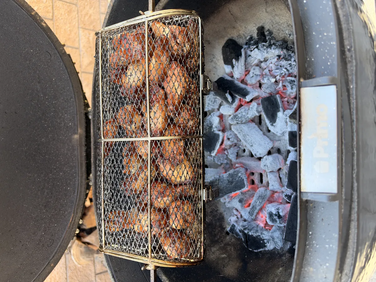 Chicken wings in a rotisserie basket cooking over glowing charcoal on a kettle grill
