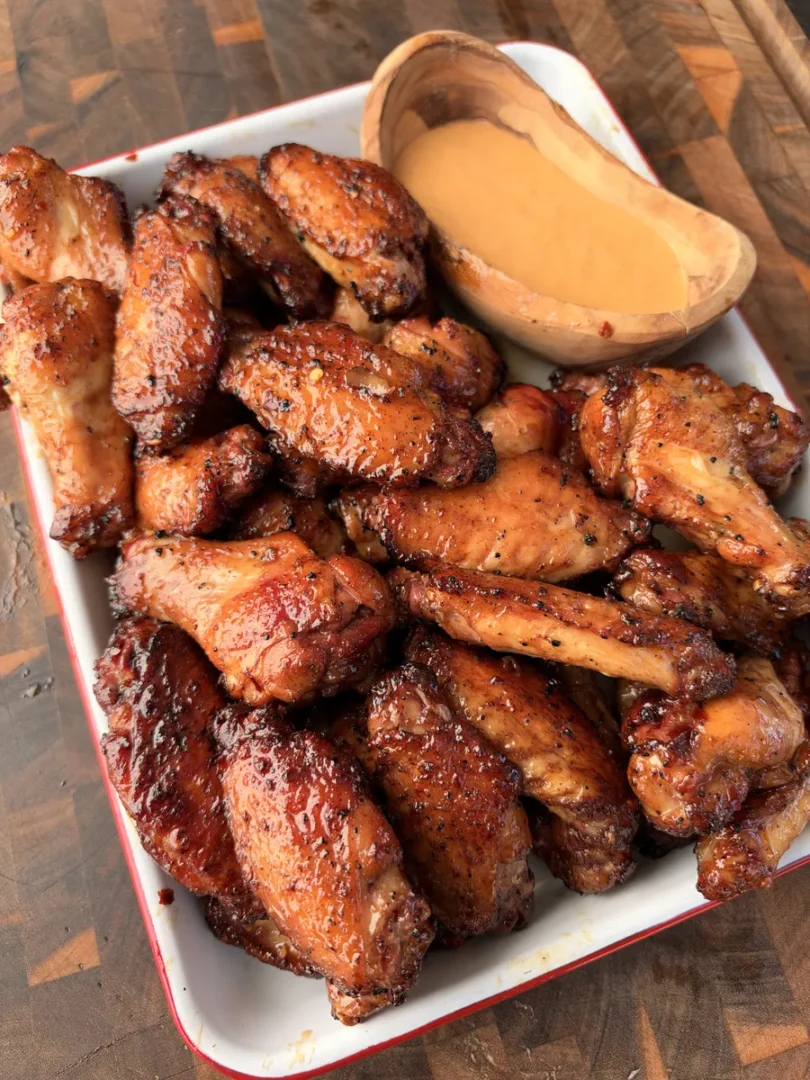 Crispy rotisserie chicken wings tossed in hot honey lime sauce piled on a white tray with a side of dipping sauce