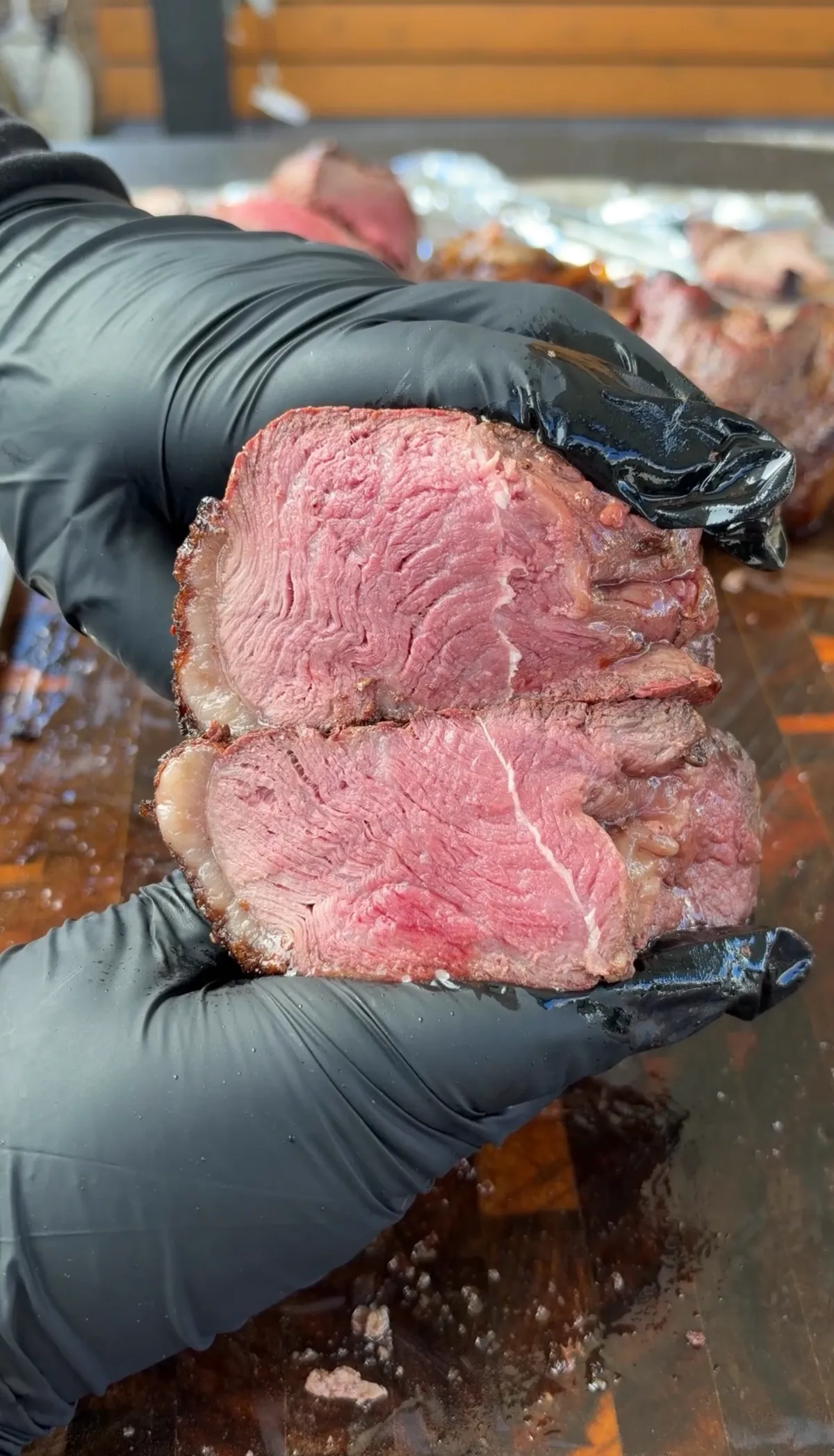 Hands in black gloves holding thinly sliced rotisserie picanha with pink interior and dark crust, ready for tacos