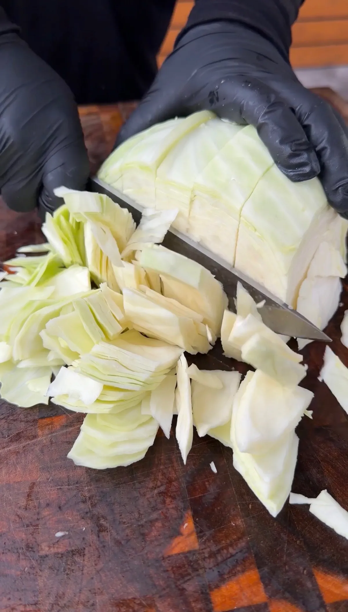 Gloved hands roughly chopping green cabbage into chunky pieces on a wooden cutting board for Dirty Cabbage recipe