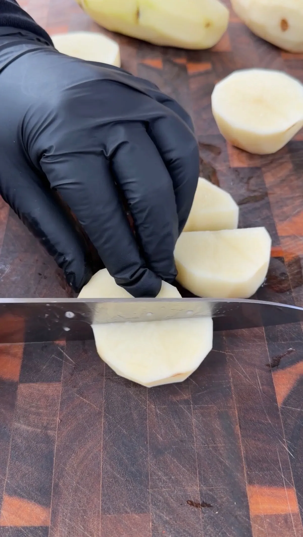 Peeled russet potatoes being cut into half-moon pieces on a wooden cutting board with a chef's knife