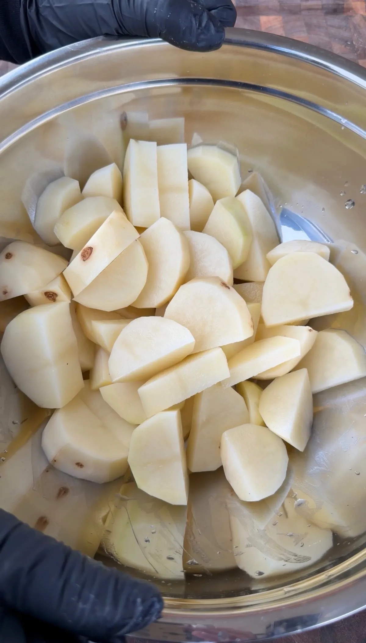 Peeled russet potatoes cut into half-moon pieces in a stainless steel bowl of cold salted water