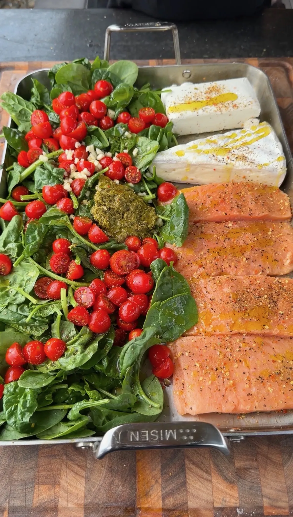 Raw salmon portions, Brie, cream cheese, cherry tomatoes, spinach, pesto, and garlic in a Misen baking pan before grilling