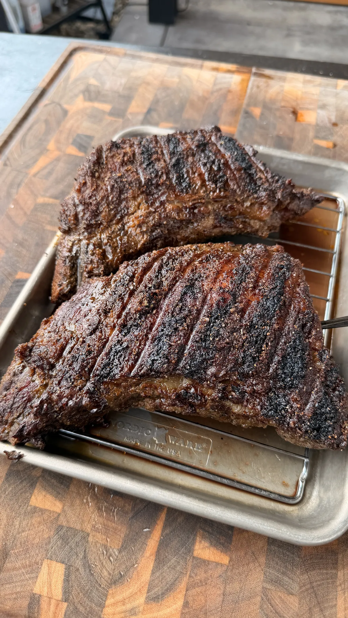 Two Santa Maria tri-tips with mud rub crust resting on a wire rack over a sheet pan after smoking over hickory