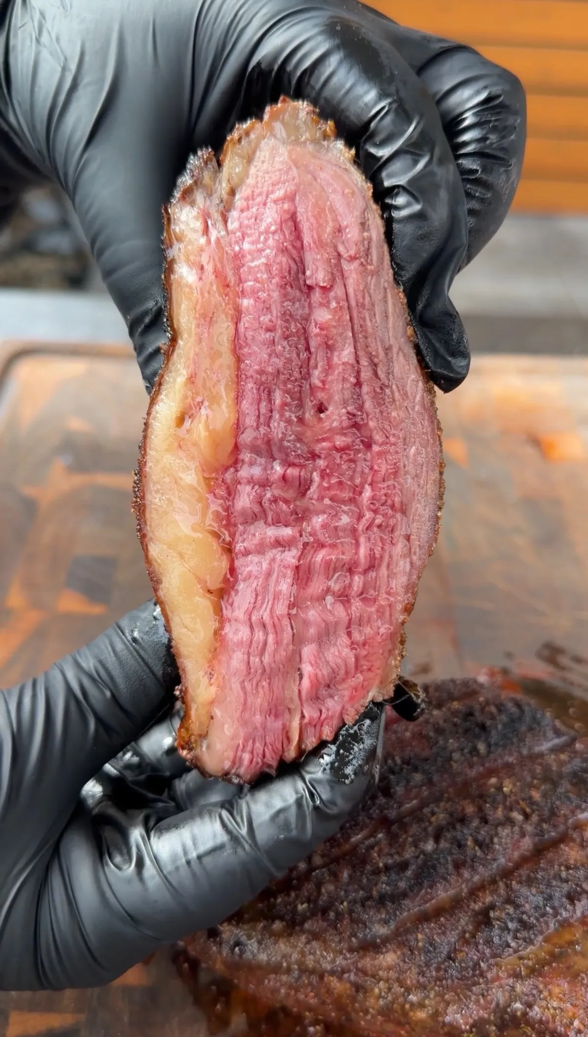 Gloved hands holding a thin slice of Santa Maria tri-tip showing pink medium-rare interior with rendered fat cap