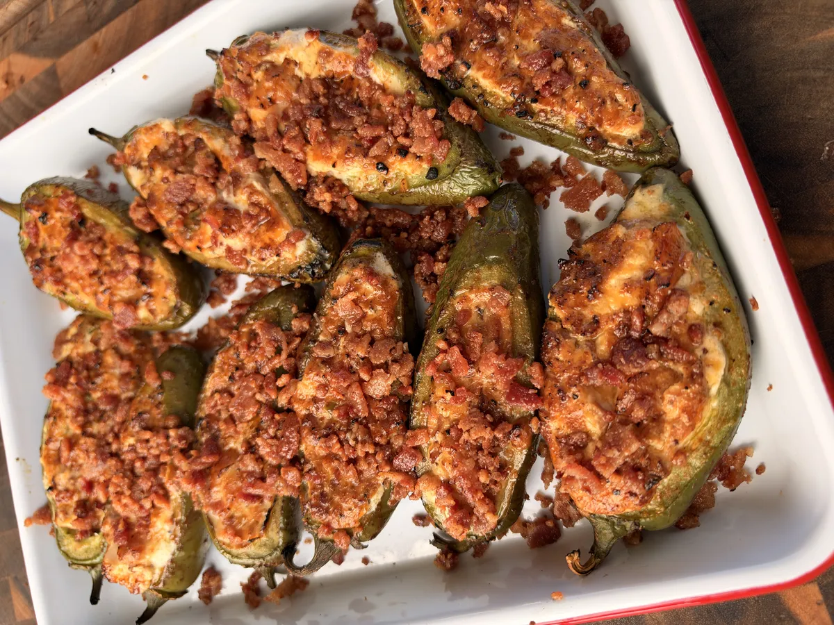 Smoked jalapeño poppers stuffed with sausage, shrimp, cream cheese, and cheddar, topped with crispy bacon bits in a white baking dish