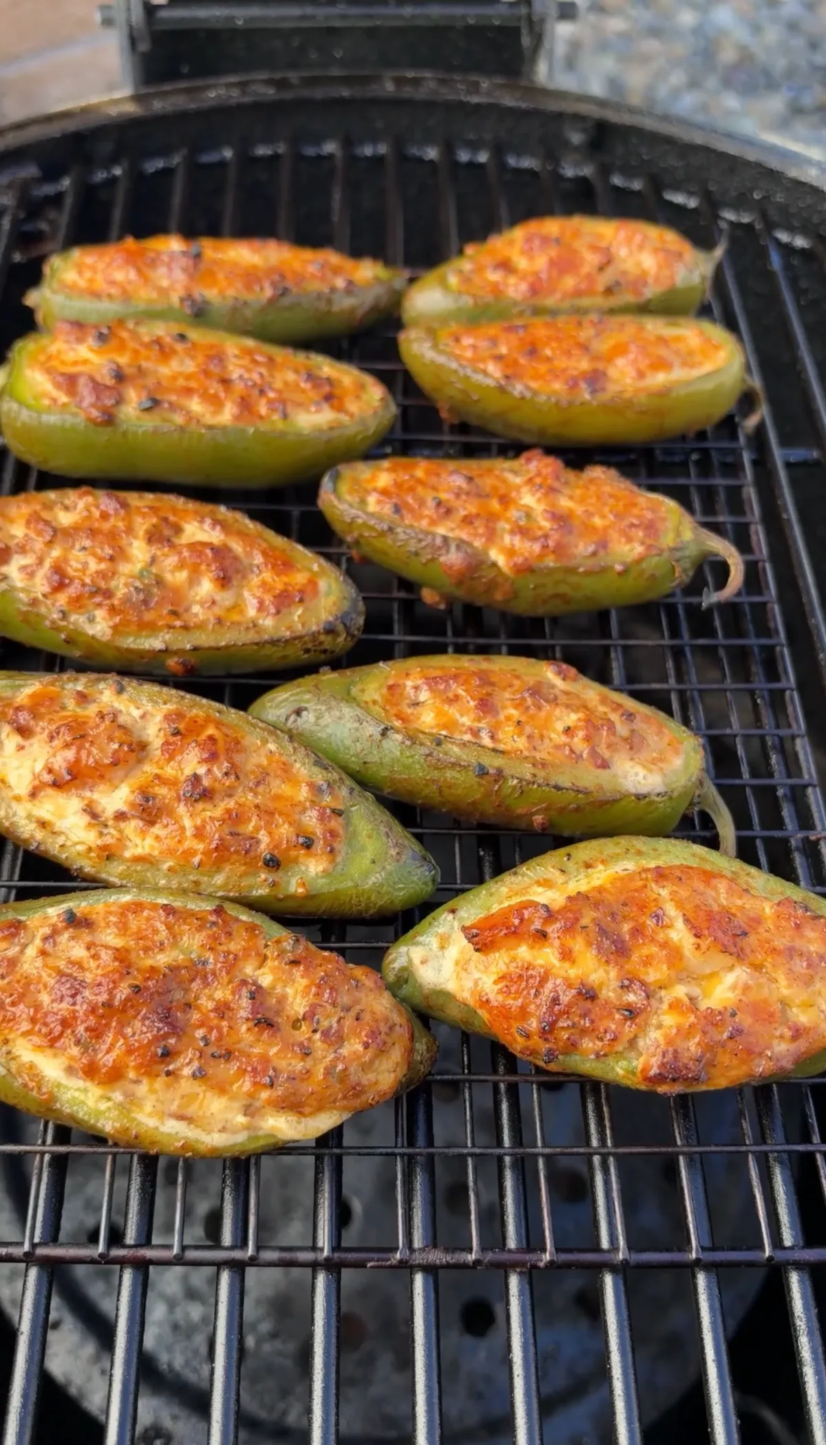 Sausage and shrimp stuffed jalapeño poppers with melted cheddar and cream cheese filling smoking on a grill grate