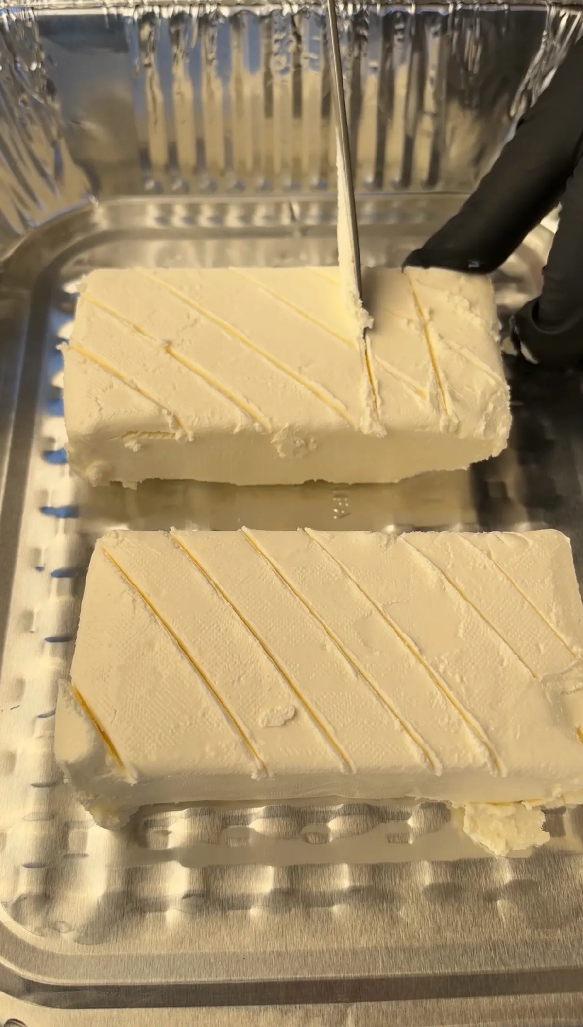 Two 8-oz cream cheese blocks scored in crosshatch pattern on foil tray, being prepared for applewood smoking