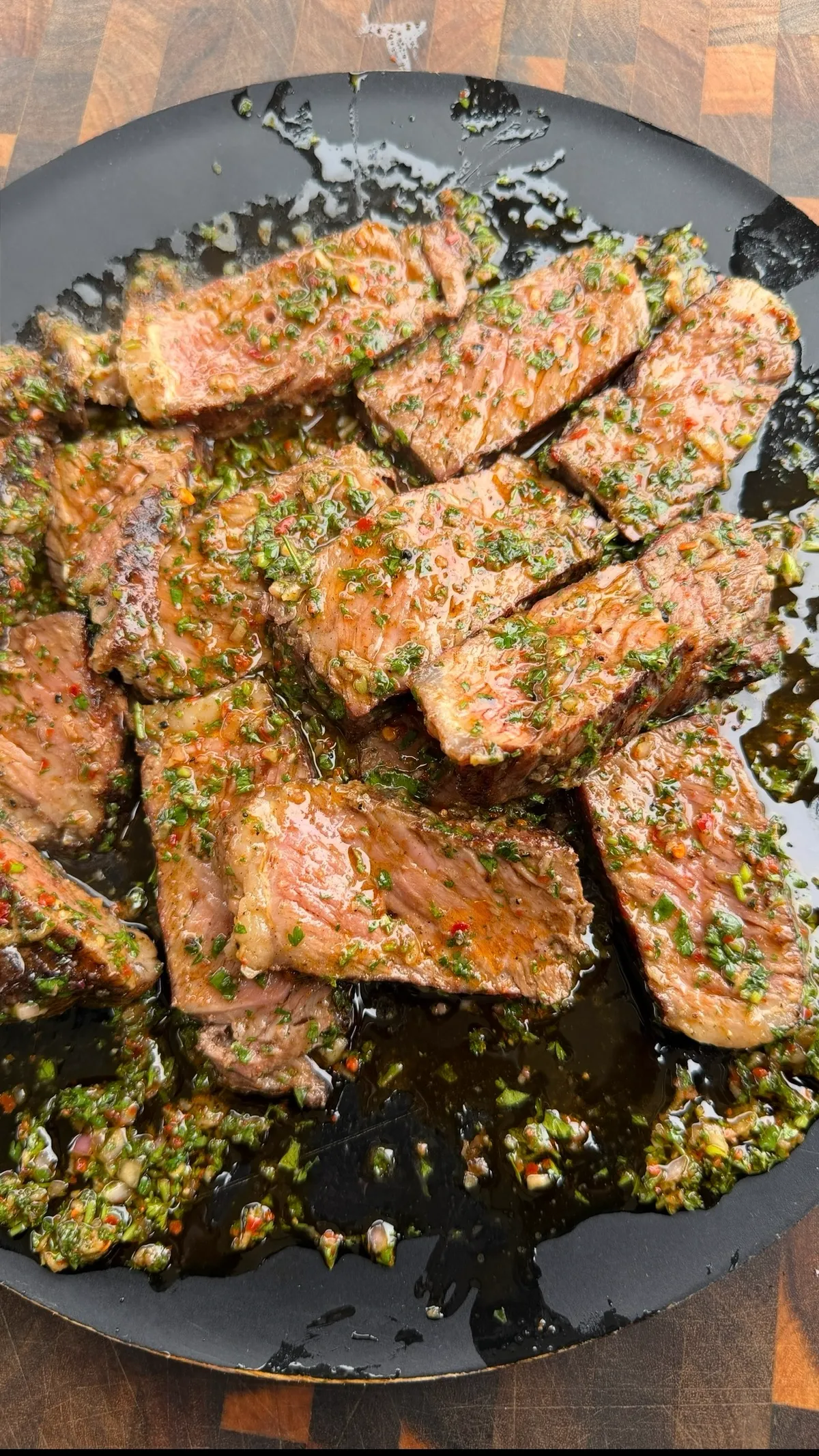 Sliced grilled New York strip steaks topped with fresh parsley and red pepper flake chimichurri on a black plate