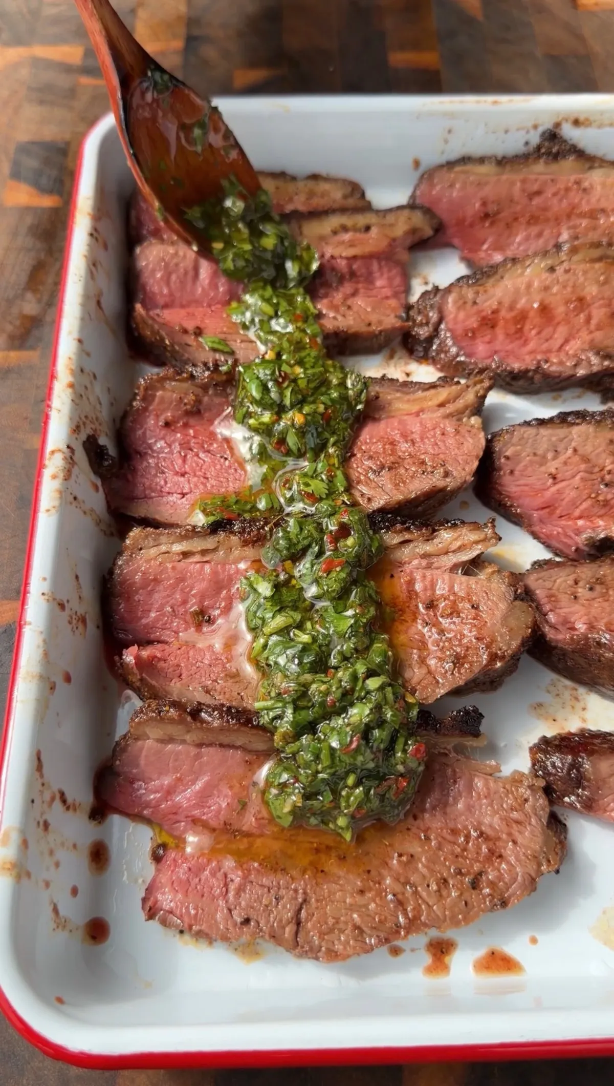 Thinly sliced Santa Maria tri-tip arranged on a white platter with fresh parsley-cilantro chimichurri spooned over the top