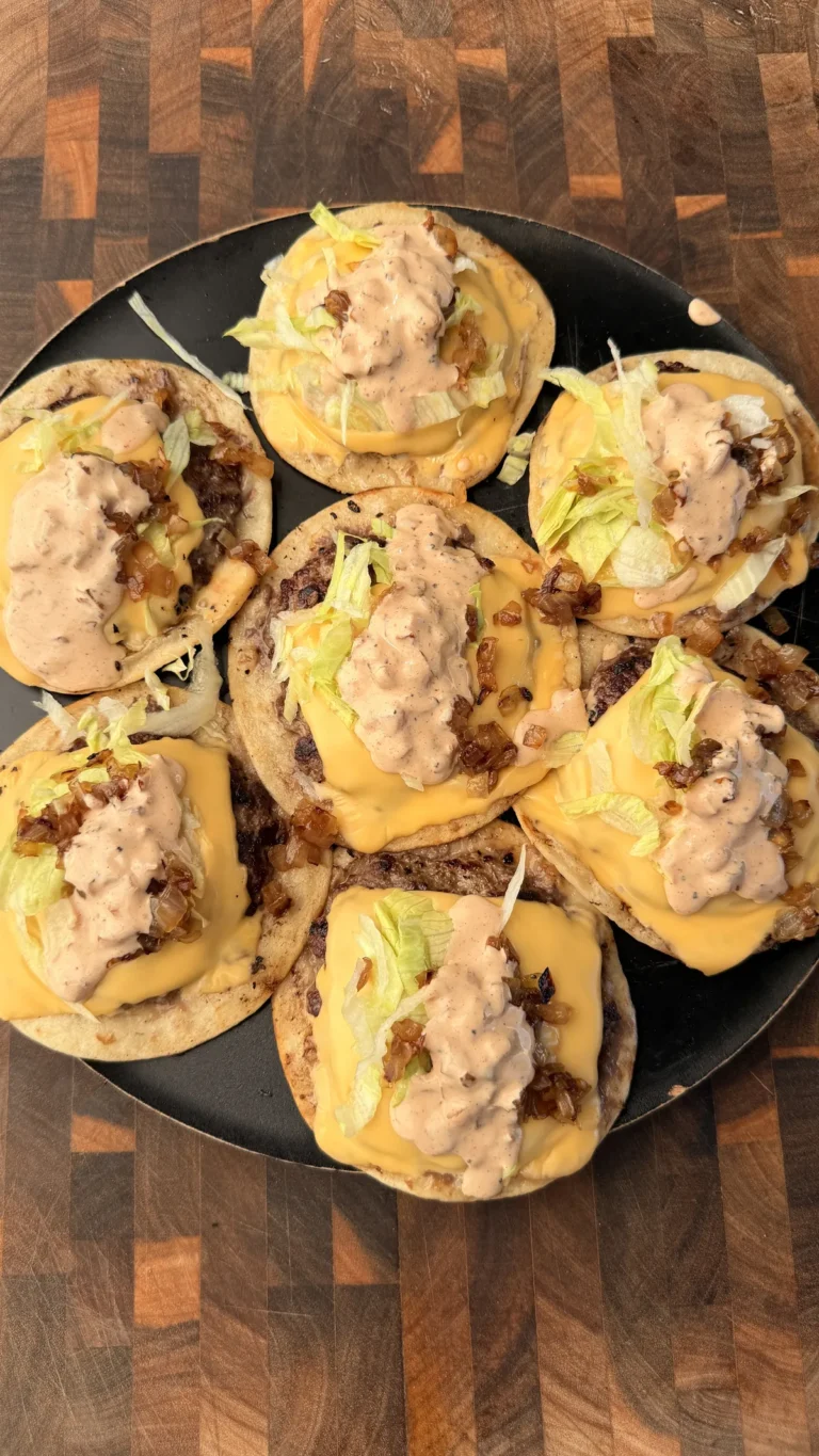 Smashburger tacos on black plate topped with melted American cheese, sautéed onions, shredded lettuce, and burger sauce