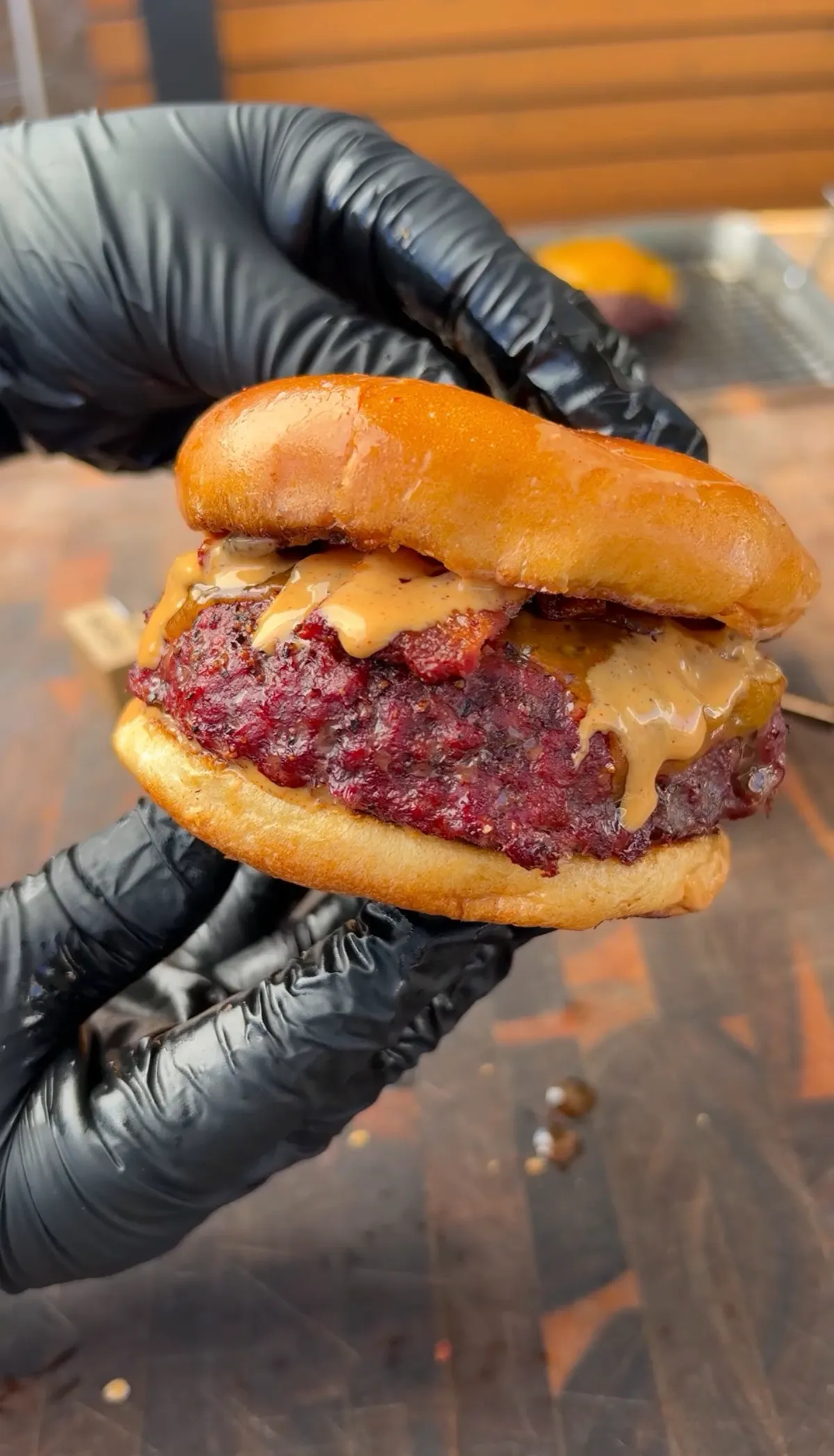 Smoked beer can burger with chipotle mayo and crispy bacon on a toasted brioche bun, held in black gloves
