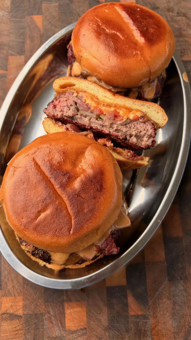Smoked beer can burgers on brioche buns with chipotle mayo and crispy bacon on a metal tray, one sliced open