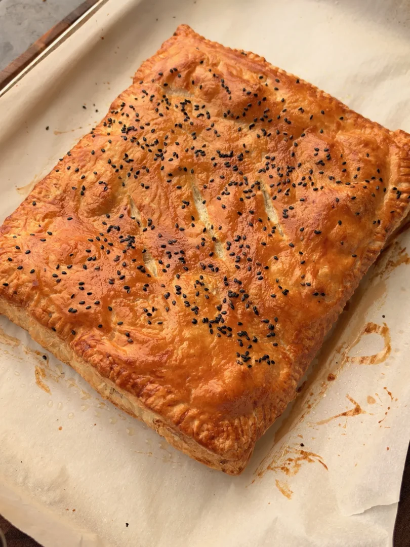 Golden baked smoked brisket stuffed puff pastry hot pocket topped with black sesame seeds on parchment-lined baking sheet