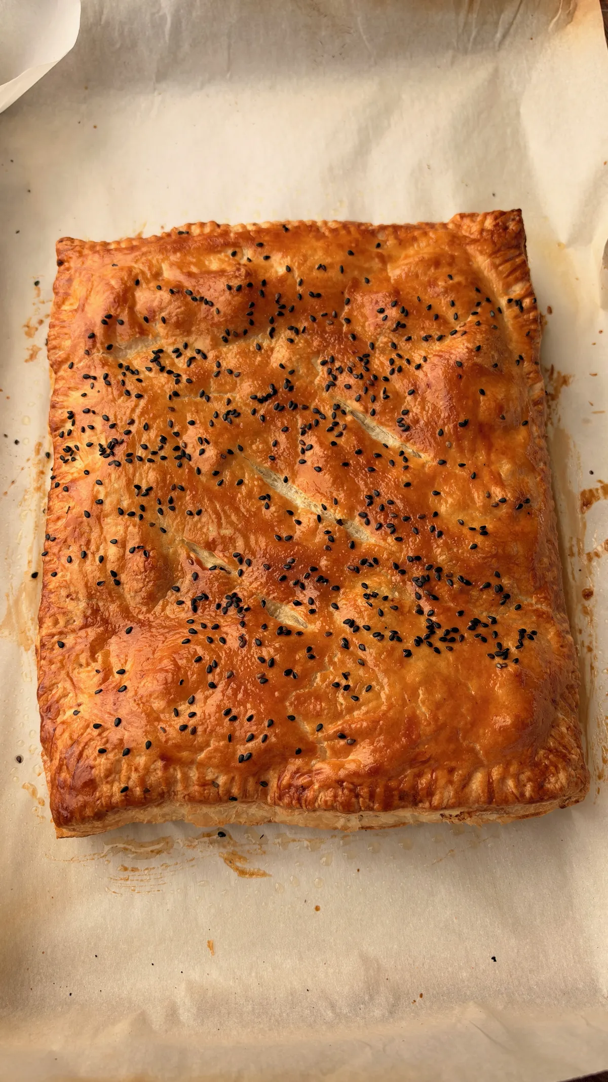 Golden baked smoked brisket hot pocket on parchment, puffed puff pastry topped with black sesame seeds and steam slits