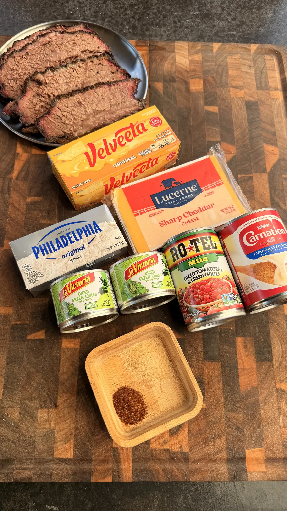 Smoked queso ingredients: sliced brisket, Velveeta, sharp cheddar, cream cheese, Rotel, green chiles, evaporated milk, and smoked paprika