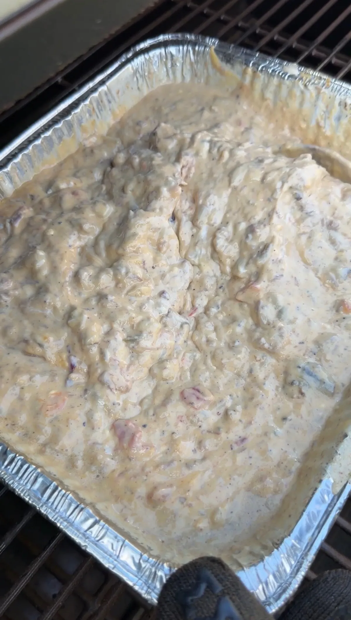 Smoked queso with chopped brisket, Velveeta, cheddar, and Rotel melting together in a foil tray on a smoker grate