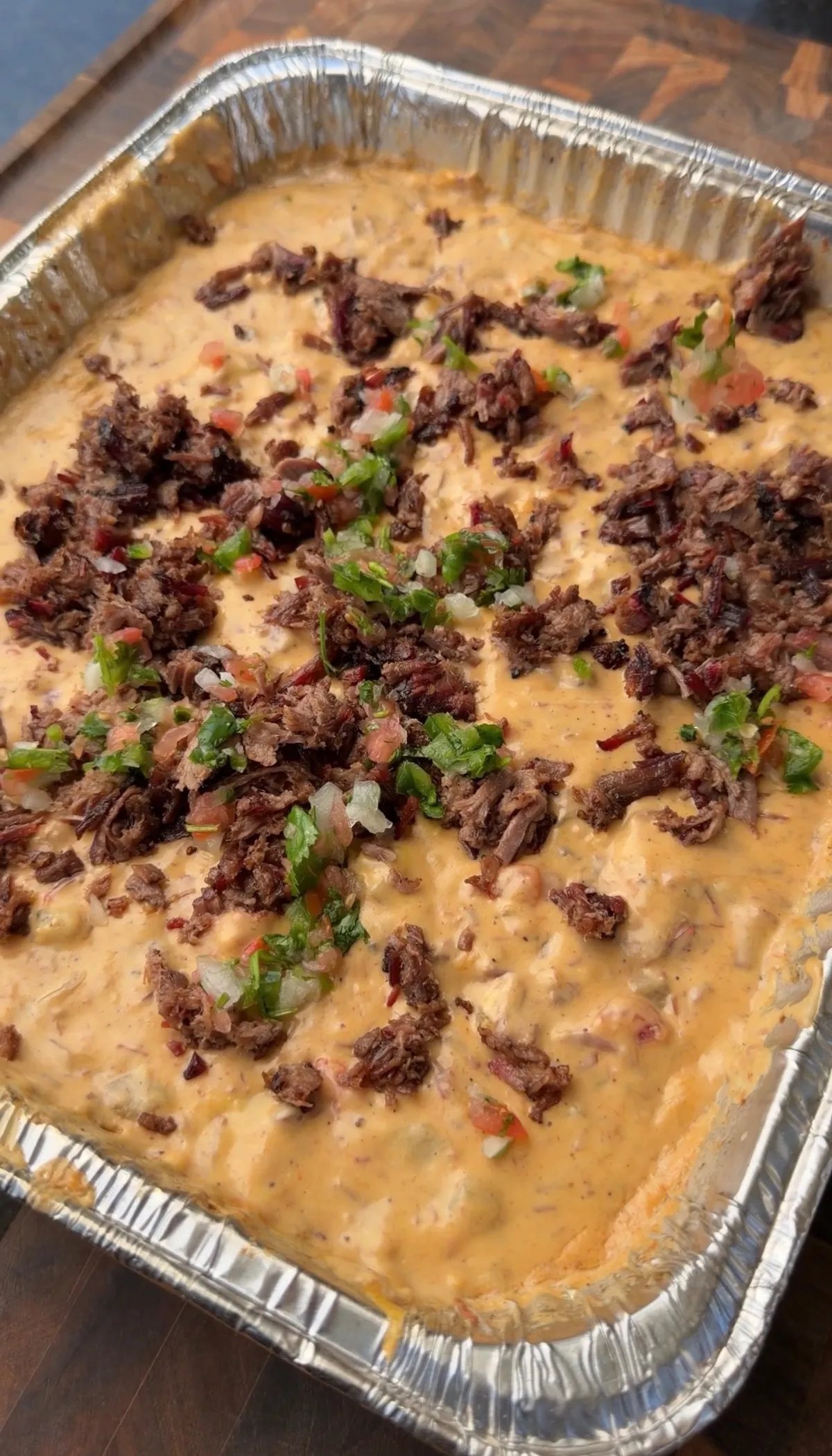 Smoked queso in foil tray topped with chopped leftover brisket, pico de gallo, and fresh cilantro