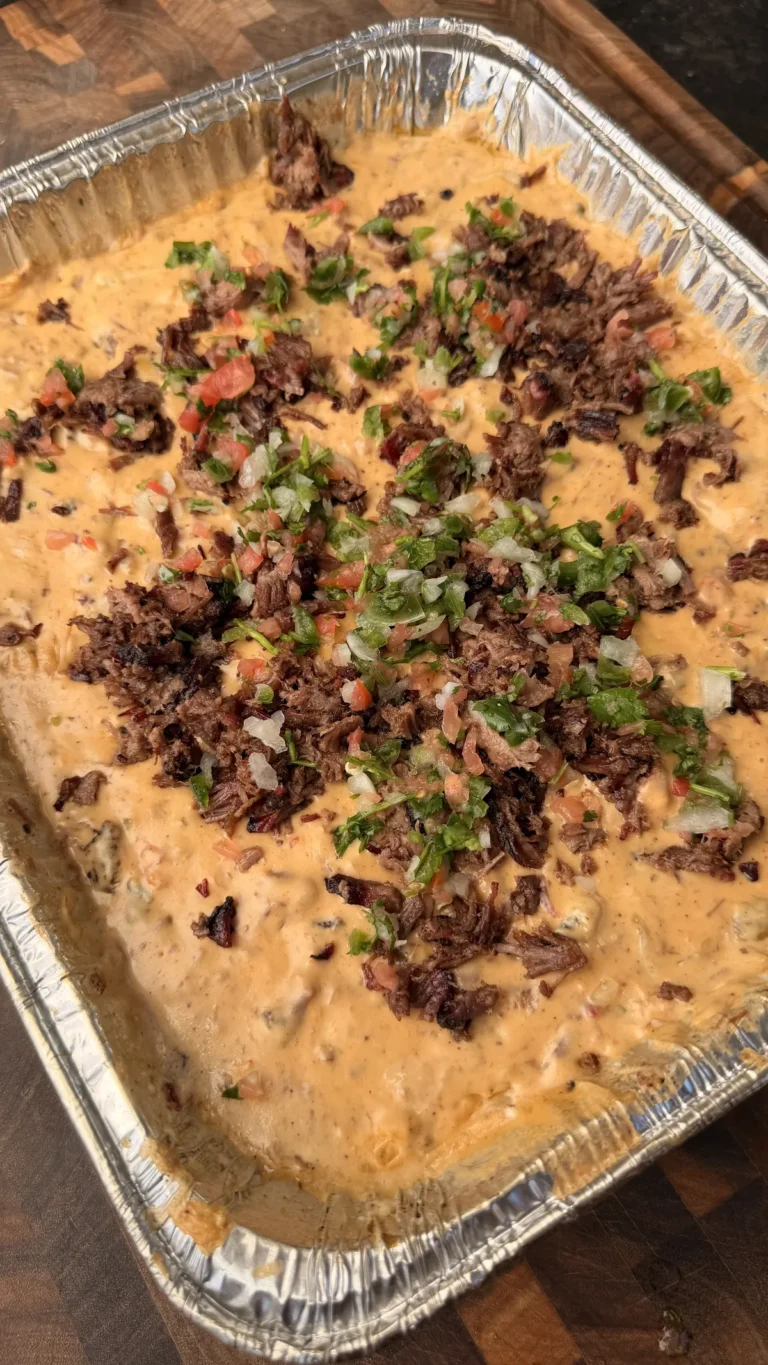 Smoked queso in foil tray topped with chopped brisket, fresh pico de gallo, and cilantro