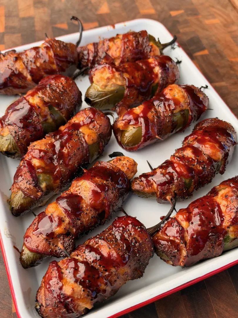 Bacon-wrapped smoked brisket-stuffed jalapeño boats with caramelized BBQ glaze on a white enamel tray