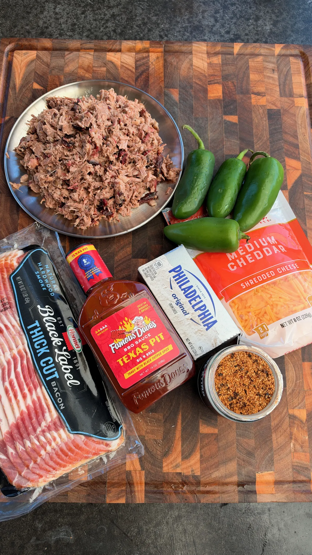 Ingredients for smoked brisket-stuffed jalapeño boats: chopped brisket, jalapeños, thick-cut bacon, cream cheese, shredded cheddar, BBQ sauce, and seasoning