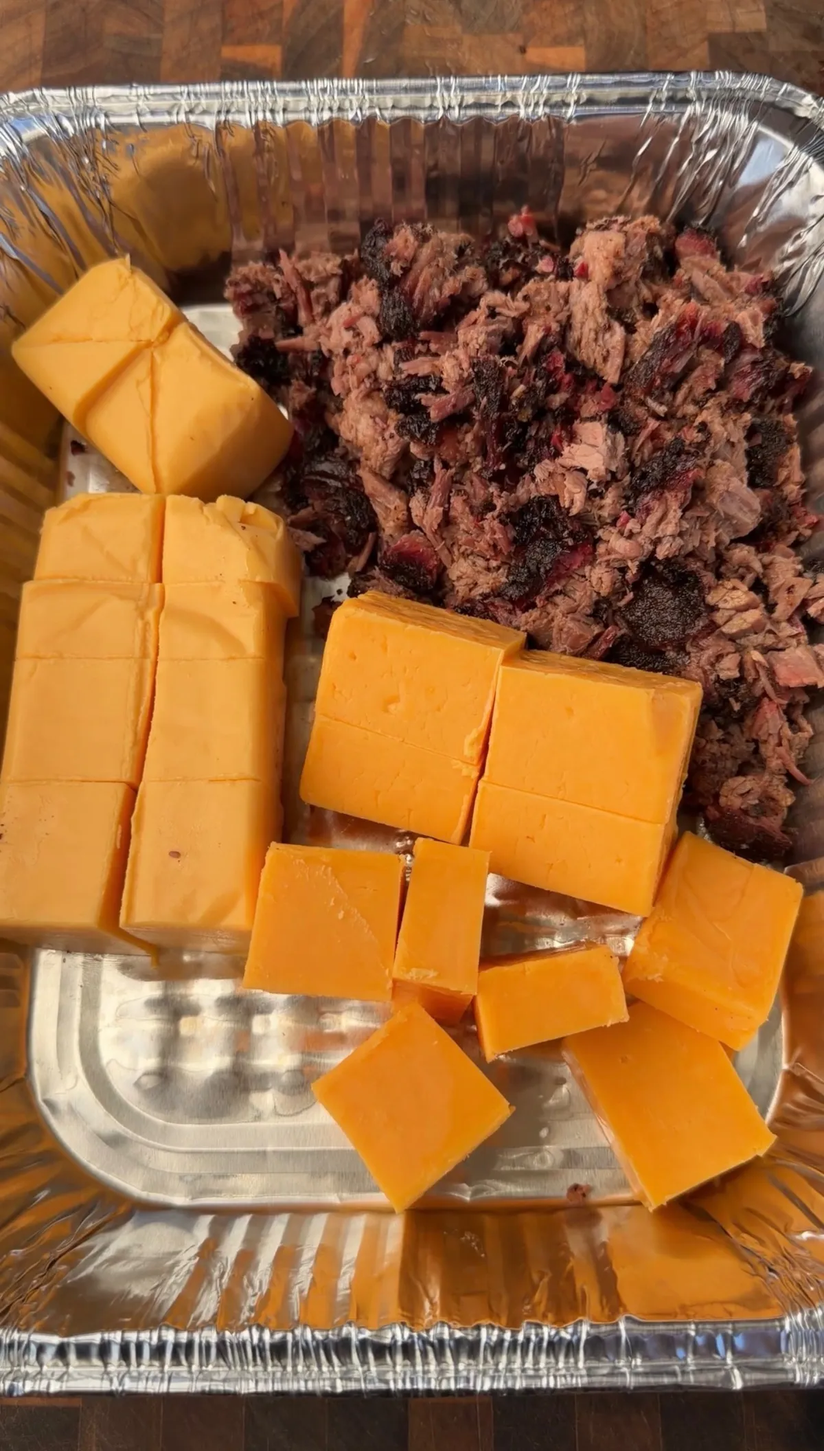 Chopped smoked brisket and cubed Velveeta and sharp cheddar cheese in a foil tray, ready to smoke