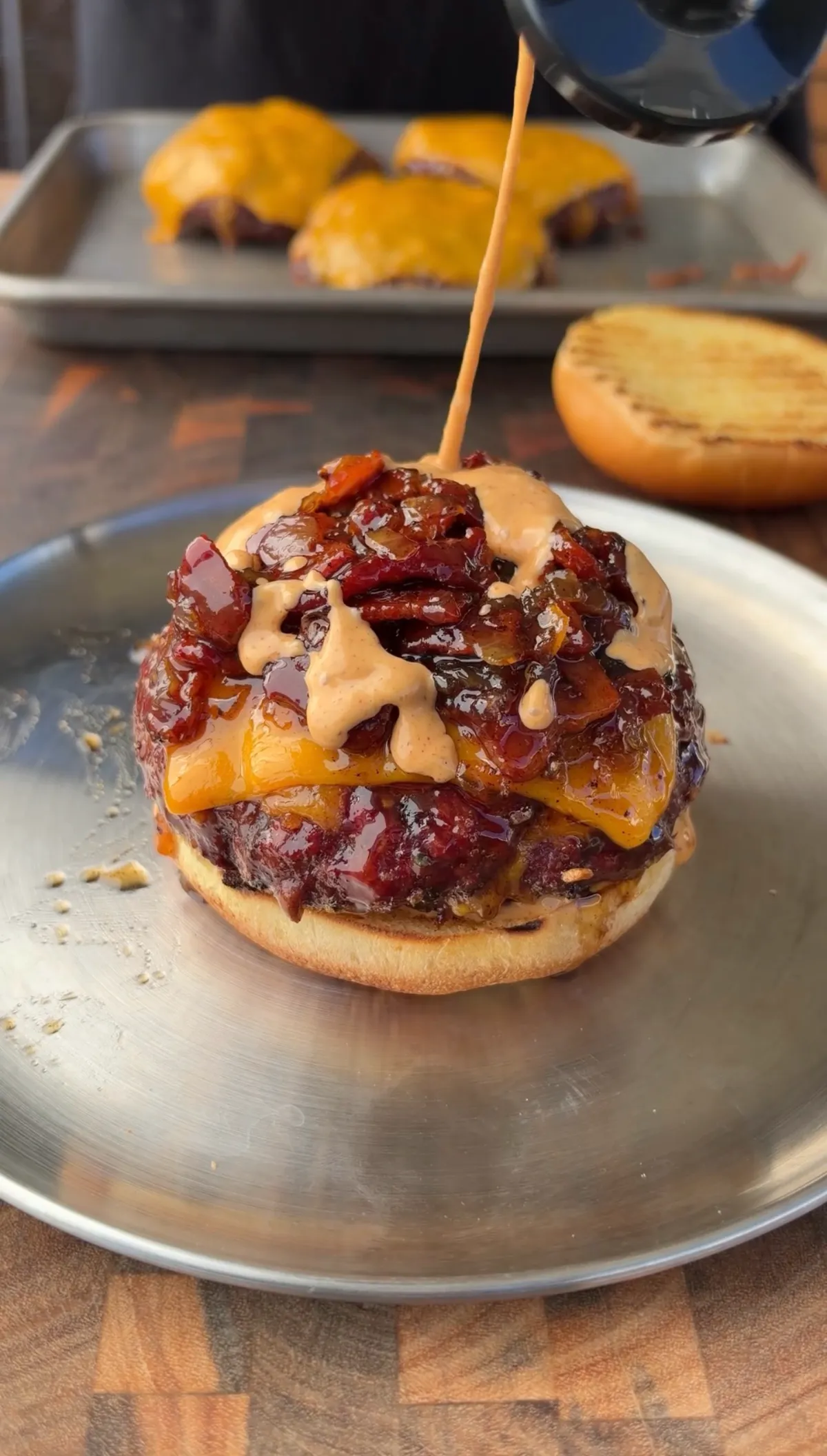 Smoked cheddar stuffed burger topped with bacon jam and chipotle mayo being drizzled on a toasted bun