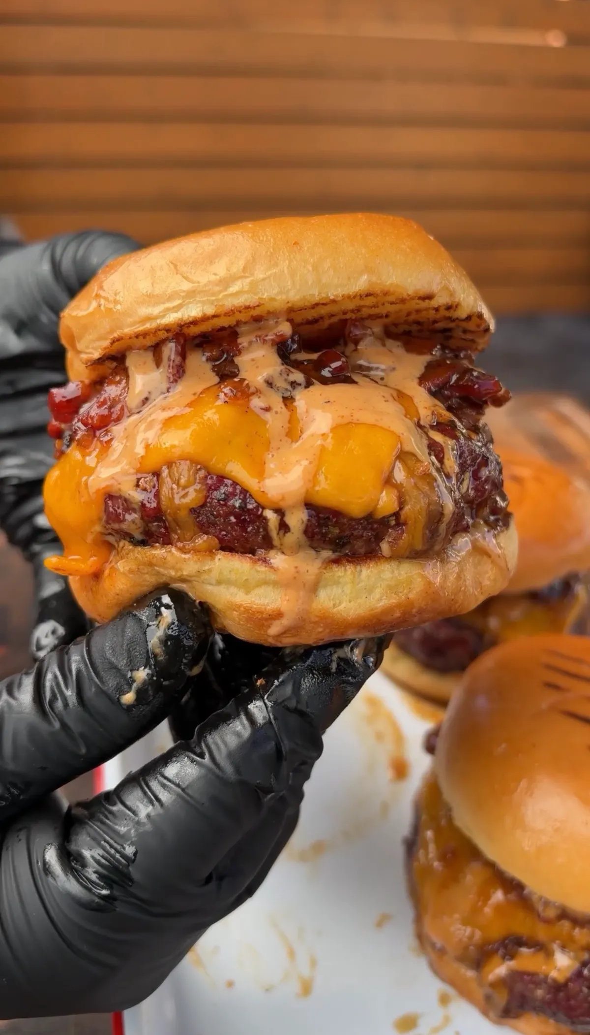 Smoked cheddar stuffed burger topped with bacon jam and chipotle mayo on a toasted bun, held in black gloves