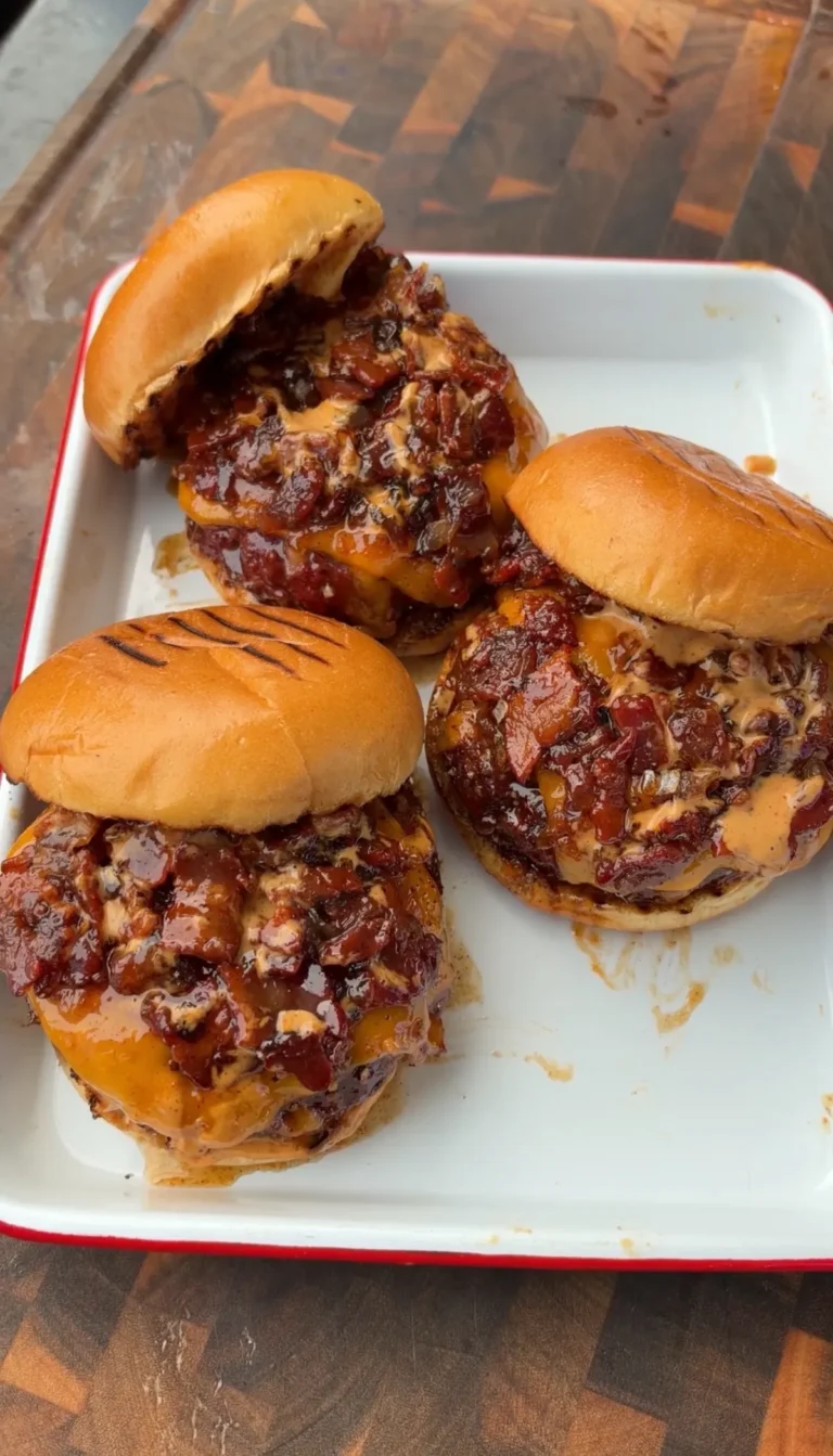 Four smoked cheddar stuffed burgers topped with bacon jam and chipotle mayo on toasted buns on a white tray