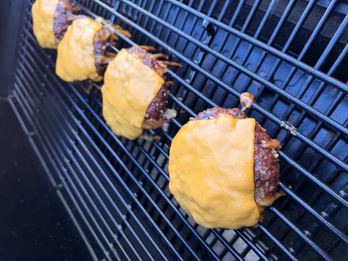 Four smoked cheddar stuffed burgers with melted cheddar cheese slices on smoker grates at 250°F