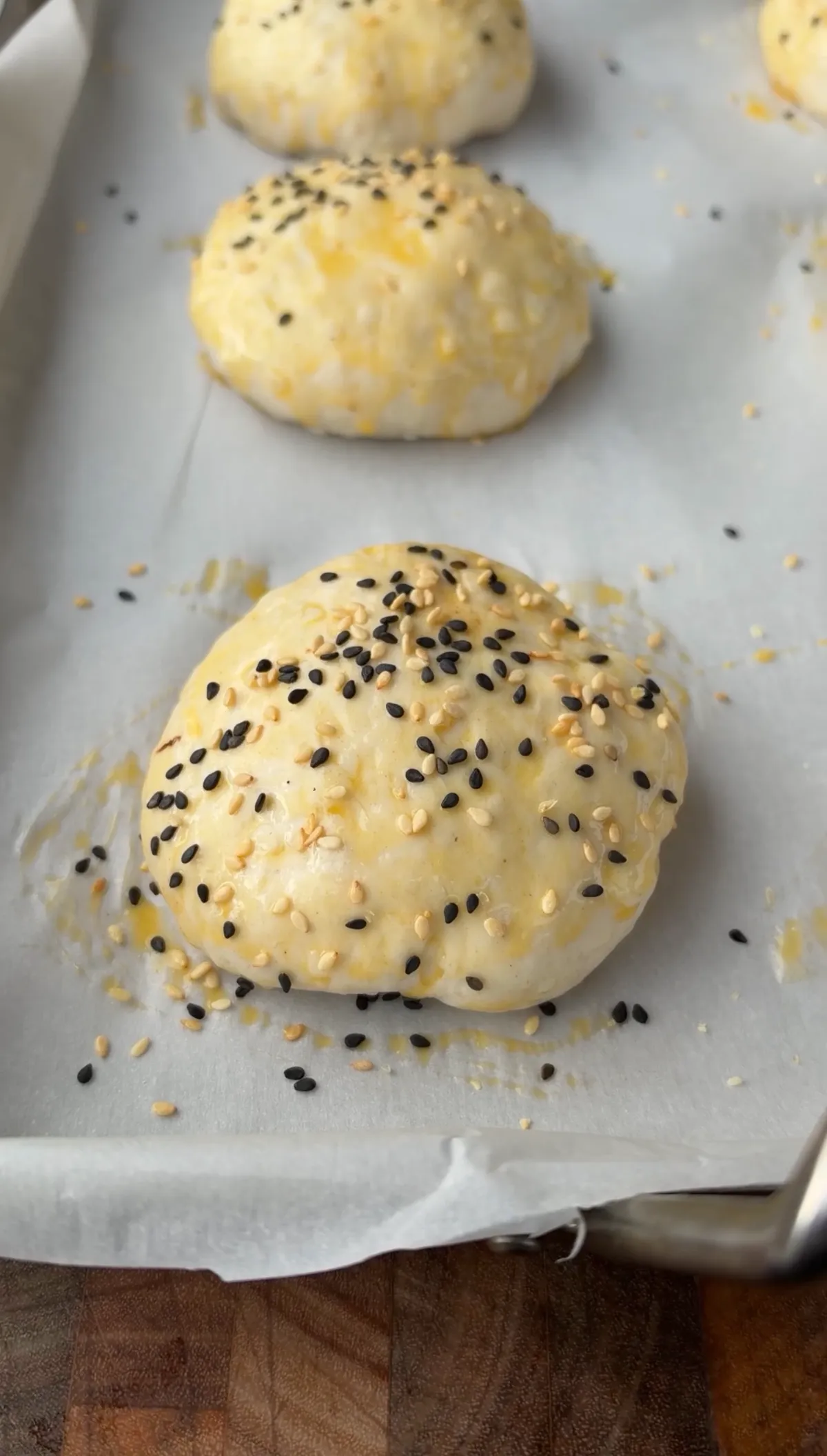 Unbaked smoked spicy cheeseburger bombs brushed with egg wash and topped with black and white sesame seeds on parchment-lined baking sheet
