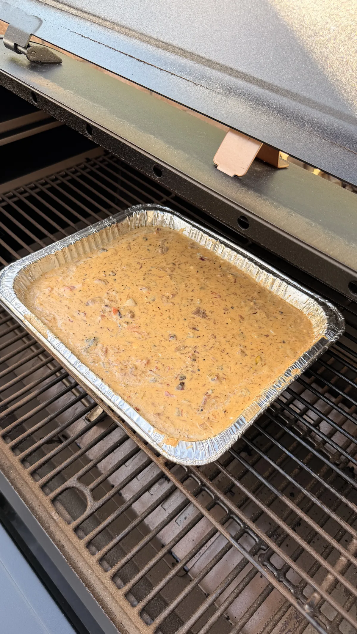 Smoked queso with brisket, Velveeta, cheddar, and Rotel in a foil tray on a smoker grill at 225°F