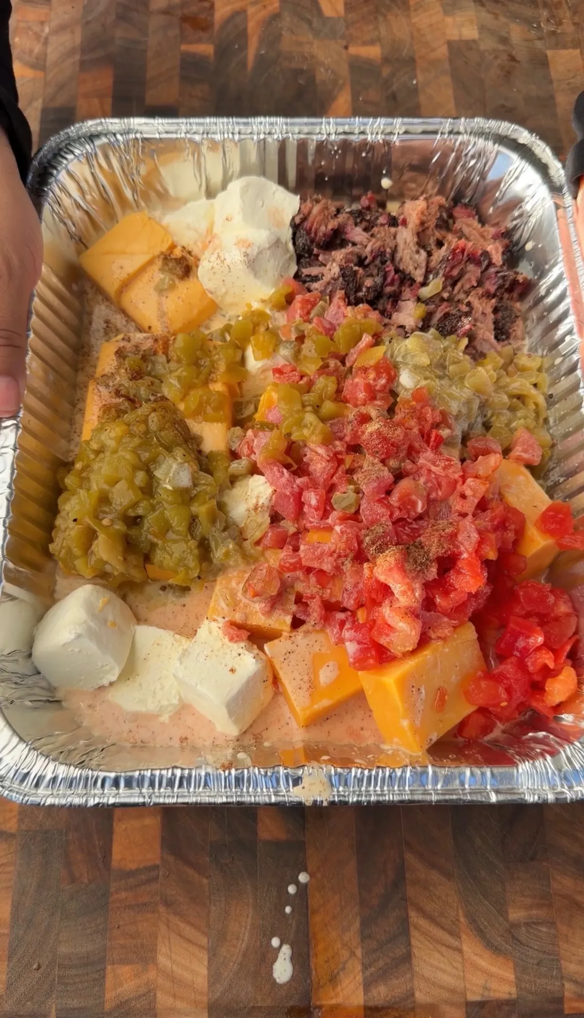 Velveeta, cheddar, Rotel, green chiles, and chopped smoked brisket assembled in a foil tray before smoking