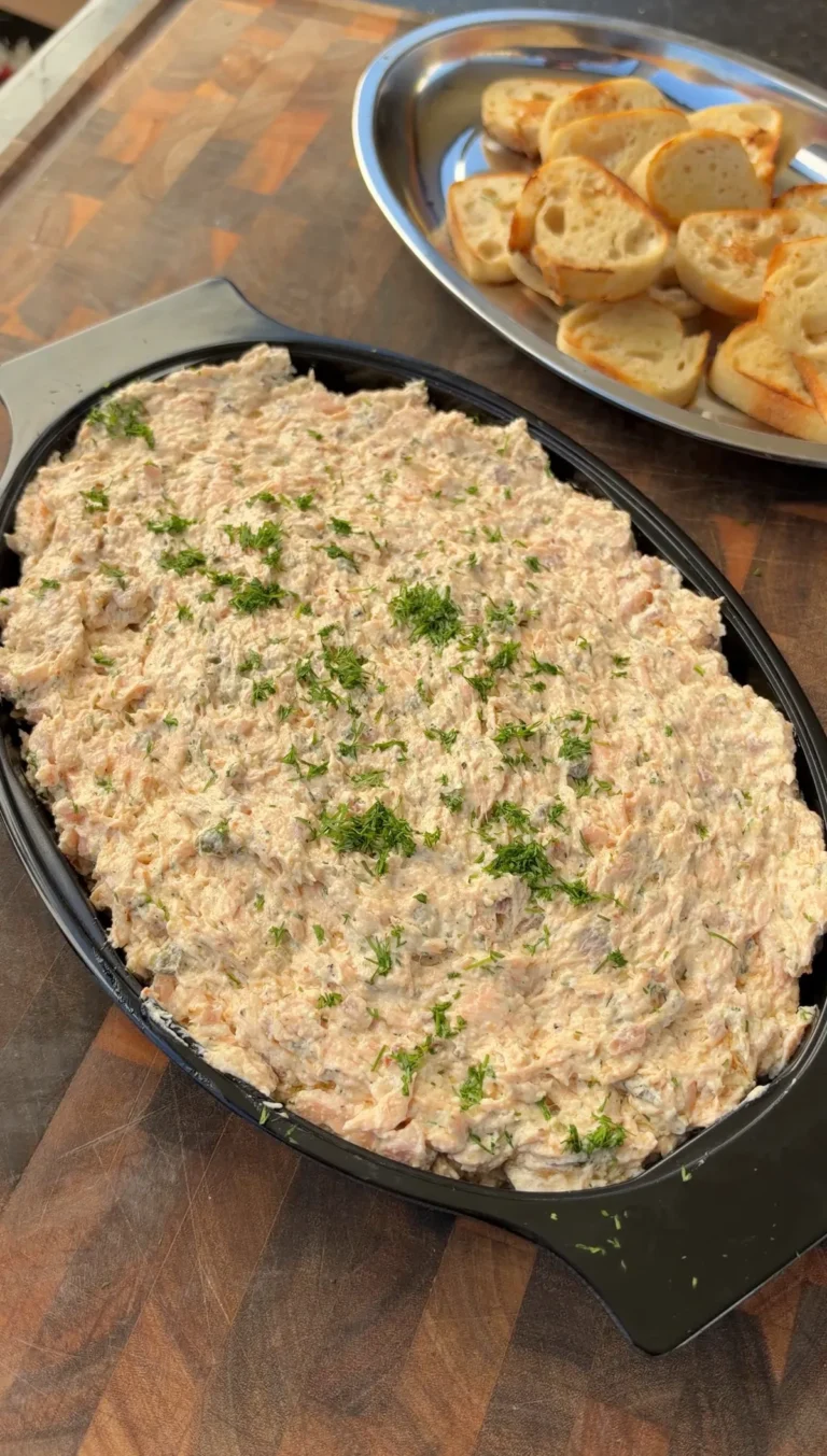 Smoked salmon and cream cheese dip garnished with fresh dill in a black dish, served with toasted bread slices
