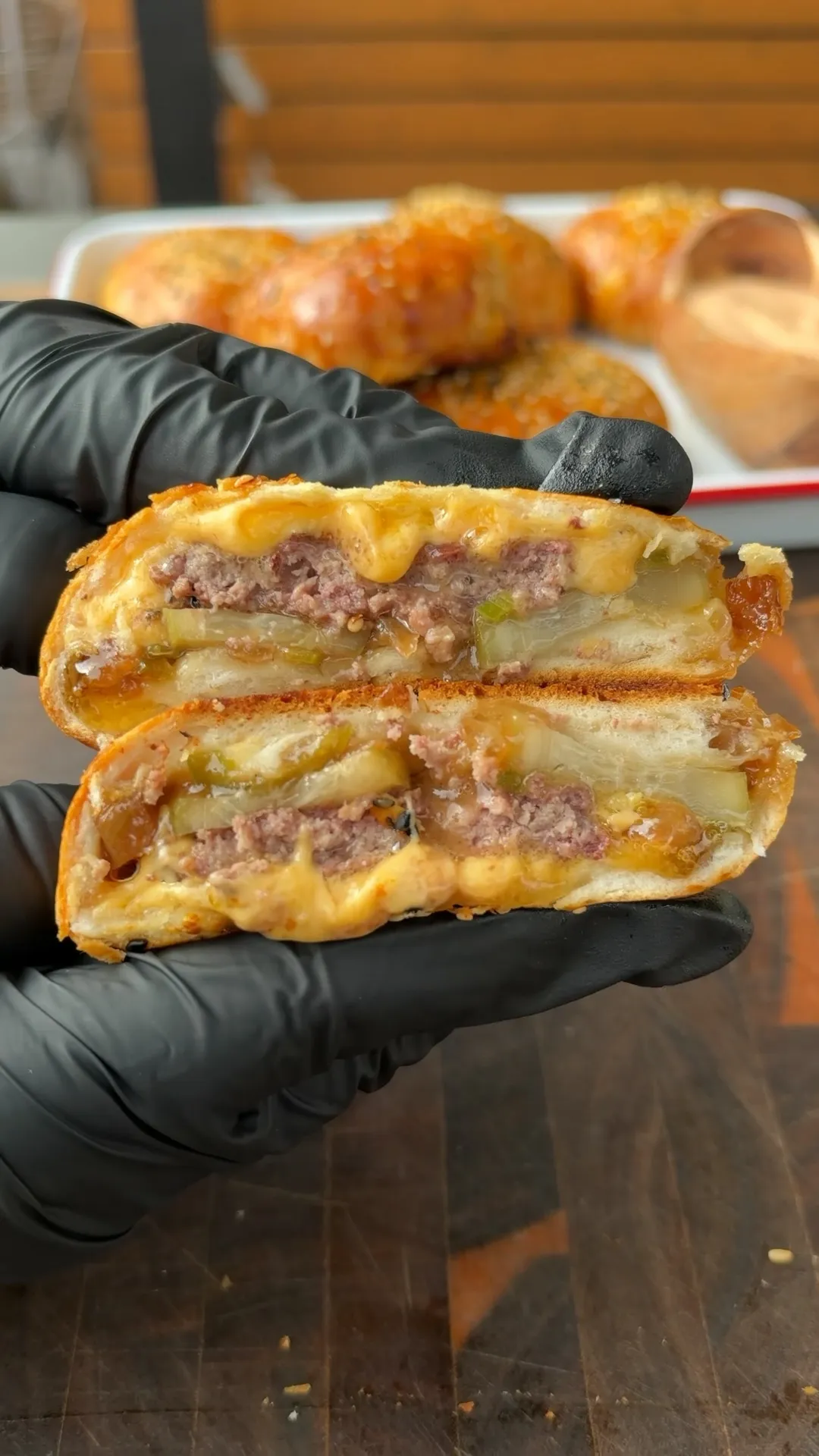 Smoked spicy cheeseburger bomb sliced in half showing melty cheddar, beef patty, pickles, jalapeños, and sautéed onions in golden biscuit dough
