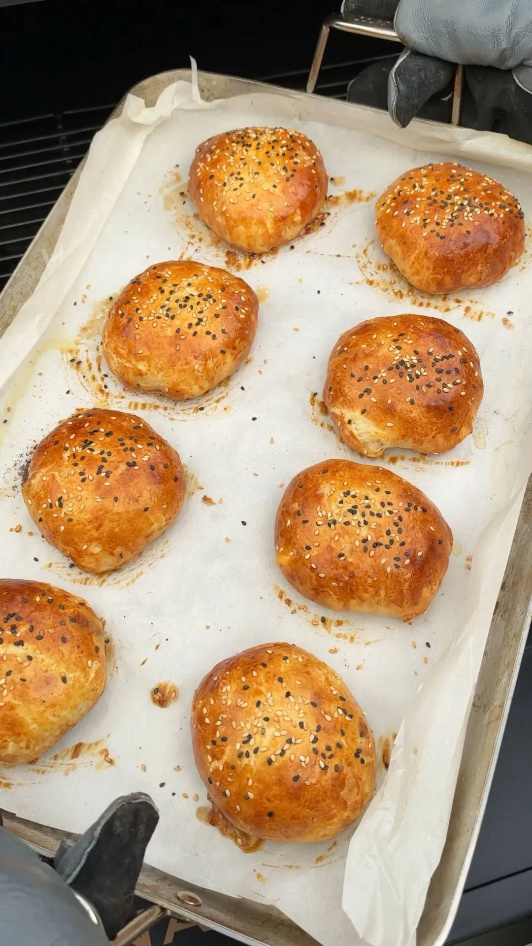 Eight golden-brown smoked spicy cheeseburger bombs topped with sesame seeds on a parchment-lined baking sheet