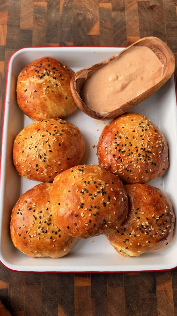 Golden-brown smoked cheeseburger bombs topped with sesame seeds in white tray with chipotle mayo dipping sauce