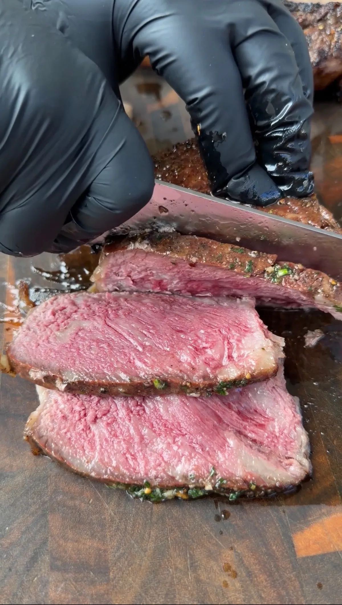 Sliced caveman-seared tomahawk steak showing pink medium-rare center with charred crust, being cut on wooden board