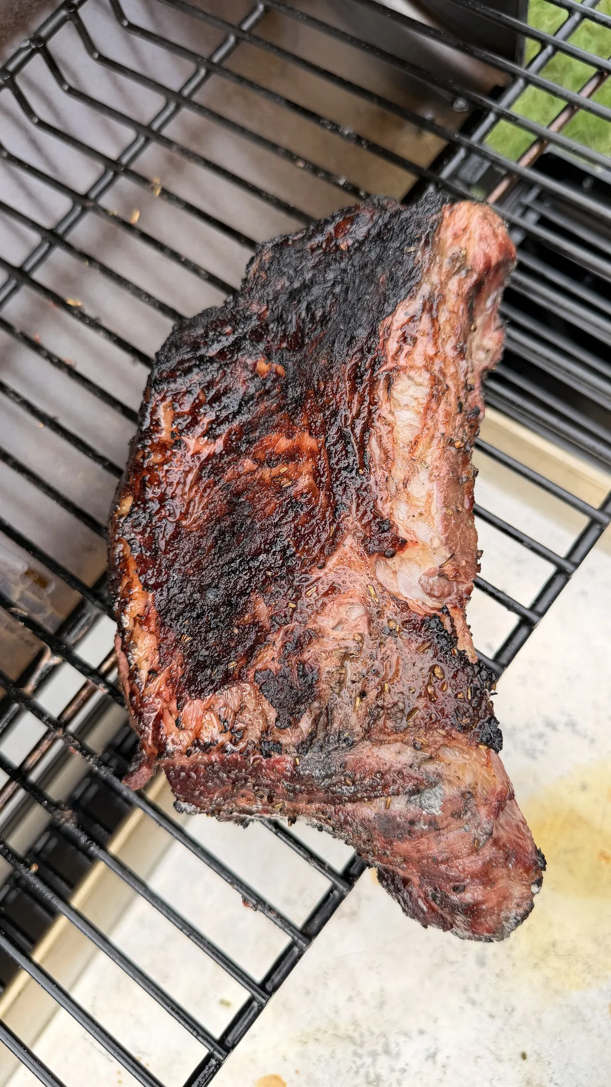 Whole smoked tri-tip with dark bark and rendered fat cap resting on smoker grate before slicing